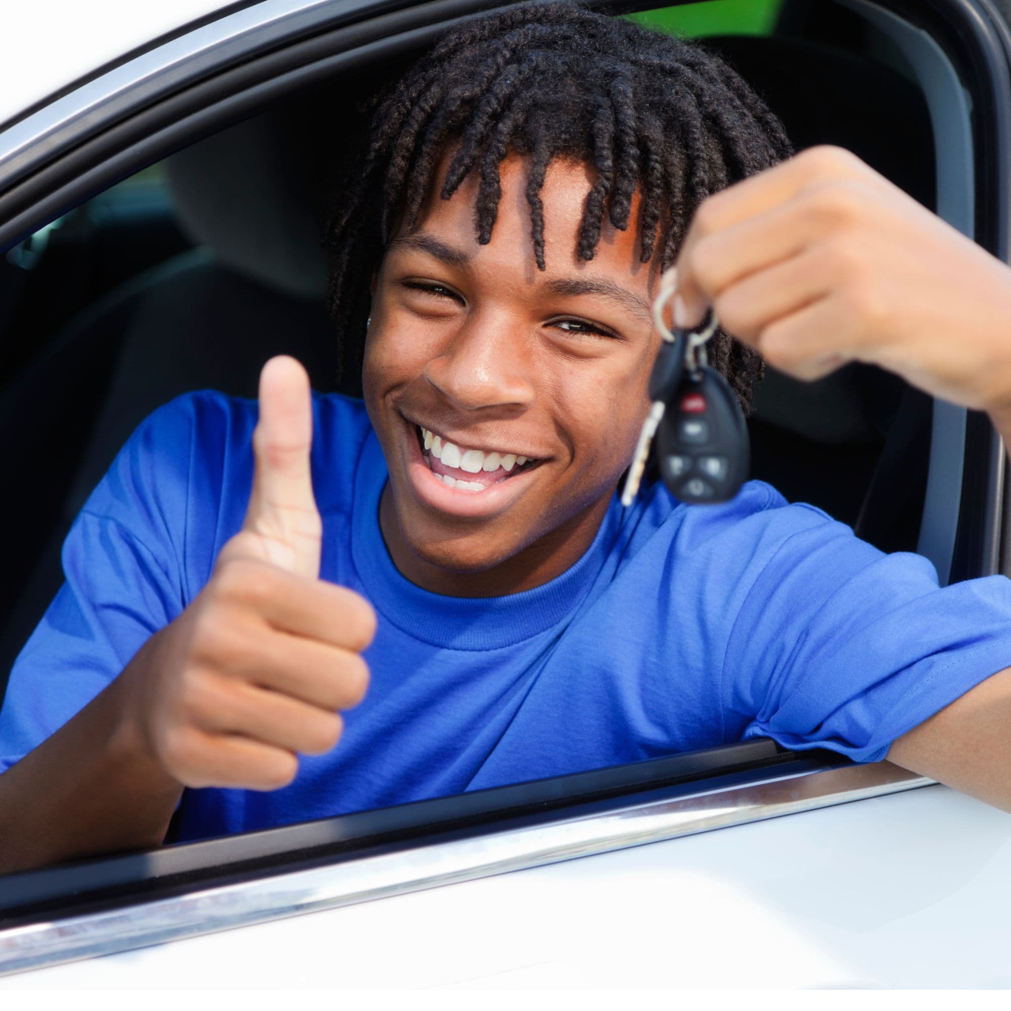 Smiling young man with dreadlocks in a car holding keys and giving a thumbs up.